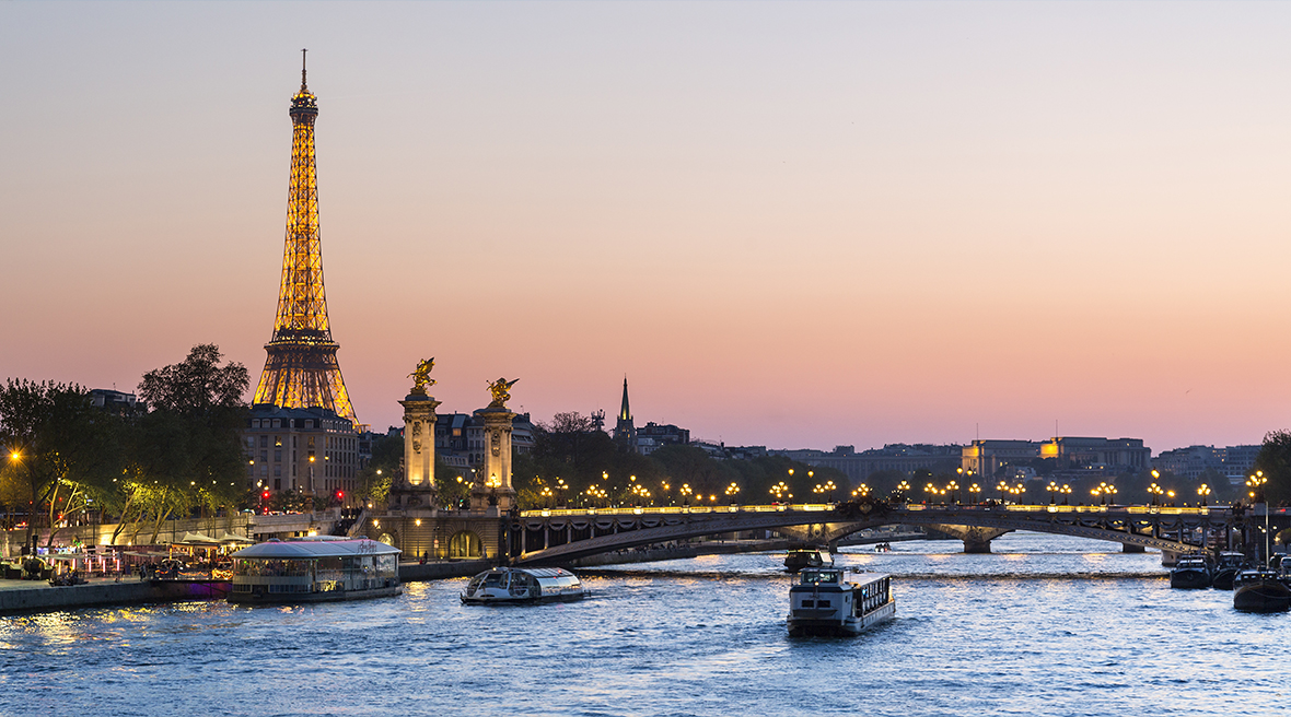 river at sunset with Eiffel Tower in the distance lit up with lights